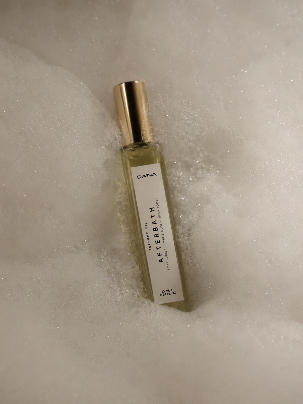 DAINA Afterbath perfume oil bottle resting in white bath foam