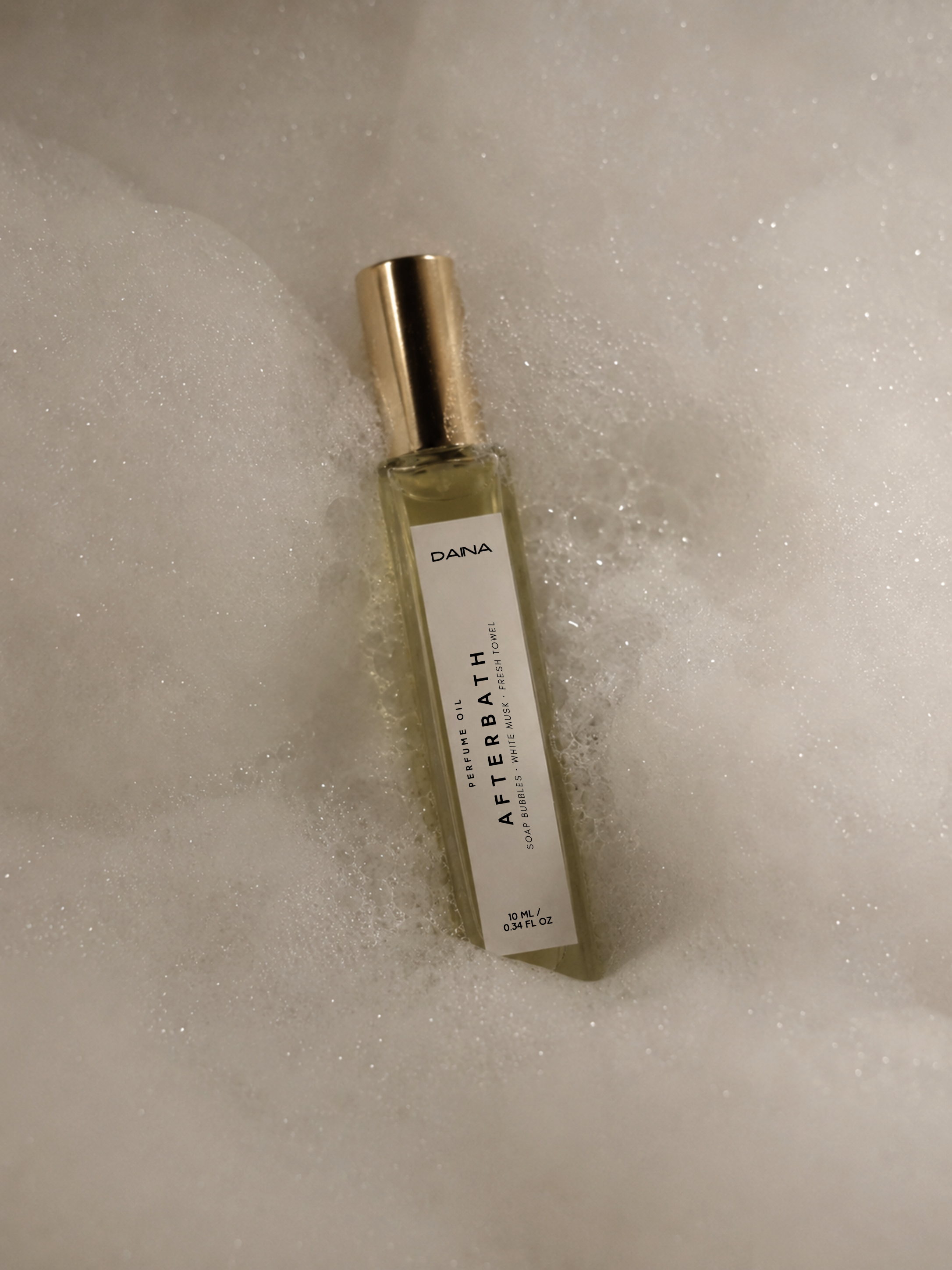 DAINA Afterbath perfume oil bottle resting in white bath foam