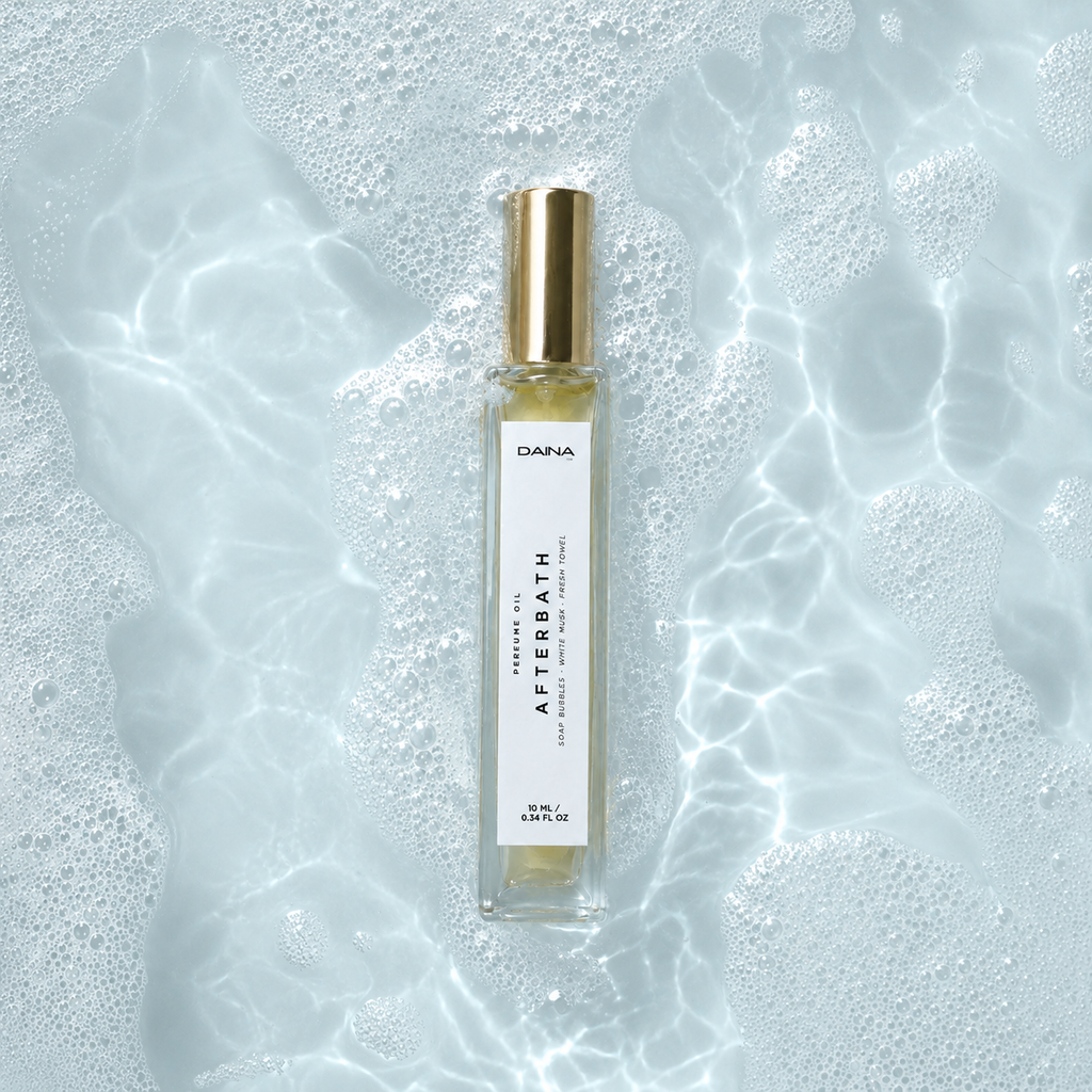 DAINA Afterbath perfume oil in pale blue bath water with soap bubbles.