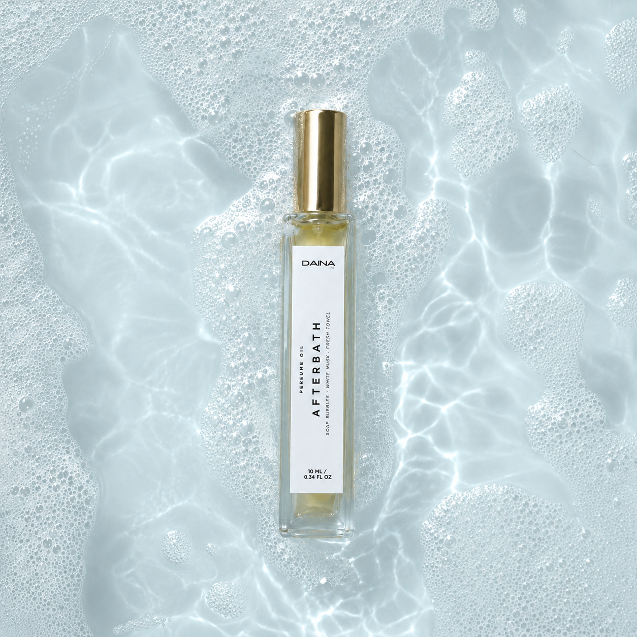 DAINA Afterbath perfume oil in pale blue bath water with soap bubbles.