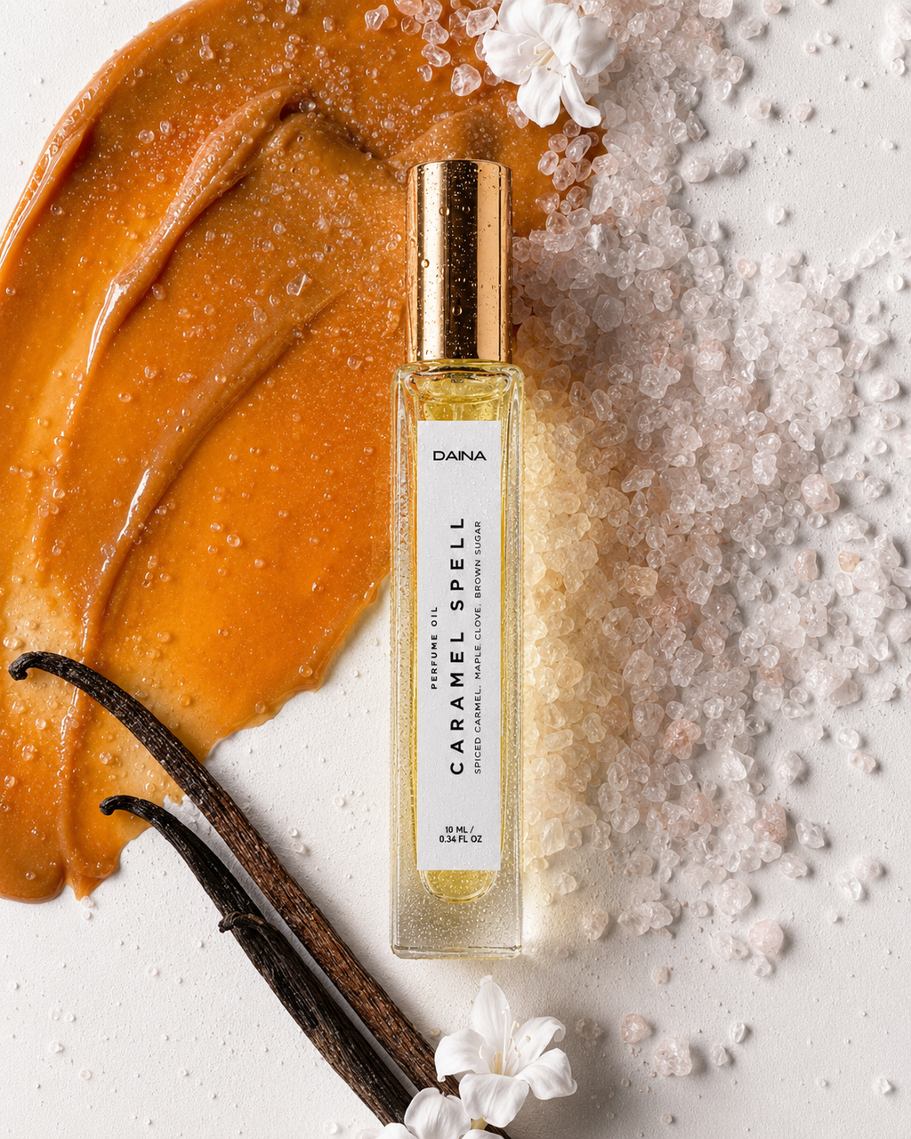 DAINA Caramel Spell perfume bottle with gold cap on caramel cream, coarse salt crystals, vanilla beans, and white flowers