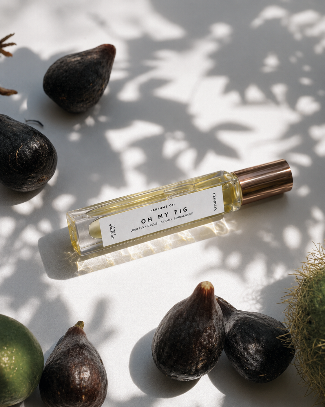 DAINA Oh My Fig perfume bottle with rose gold cap, styled with fresh figs under dappled shadow light