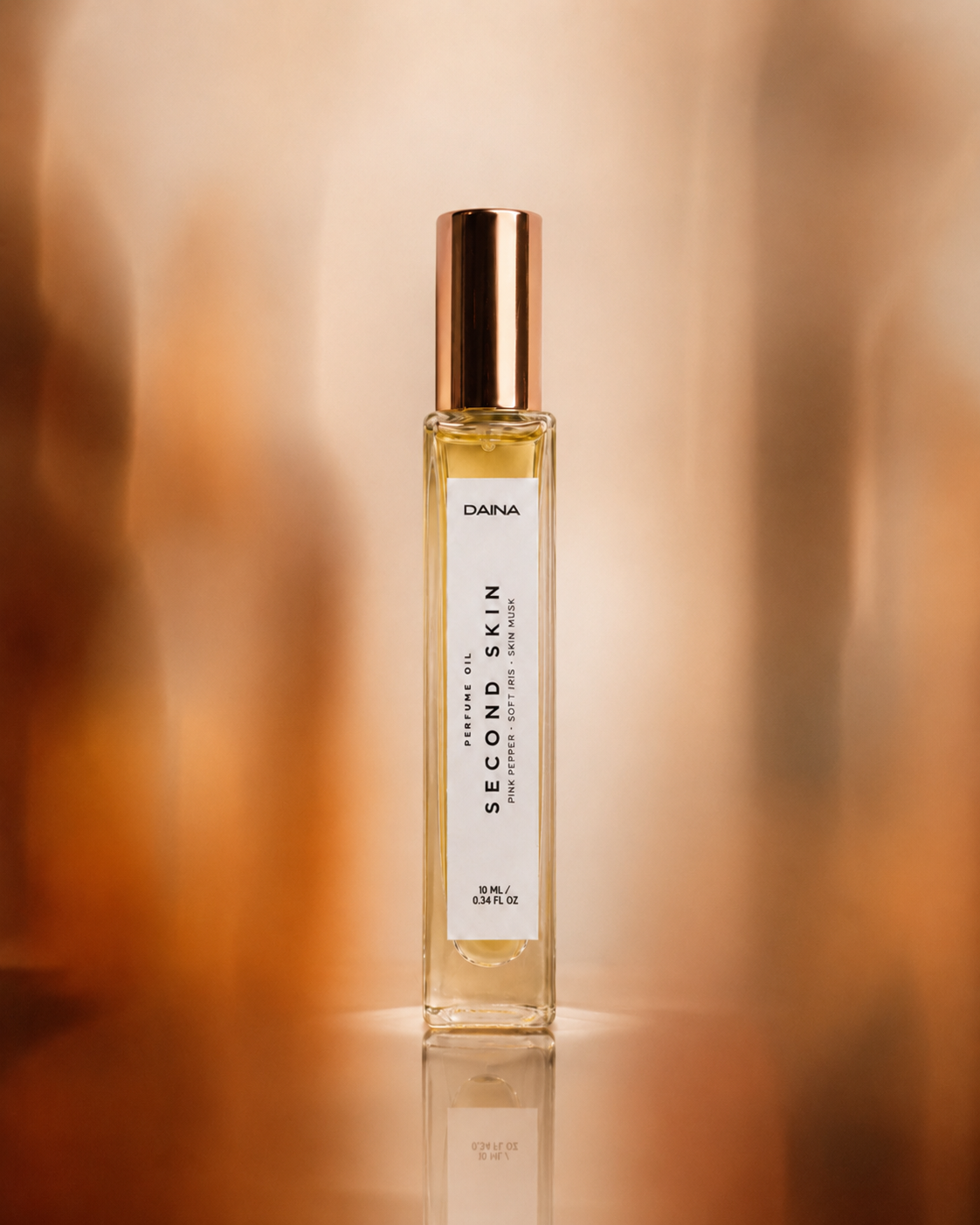 DAINA Second Skin perfume bottle with gold cap against a warm blurred orange-brown background