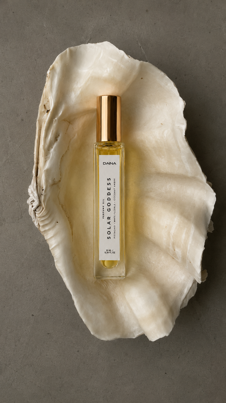 DAINA Solar Goddess perfume bottle with gold cap resting in an open clam shell on a gray surface