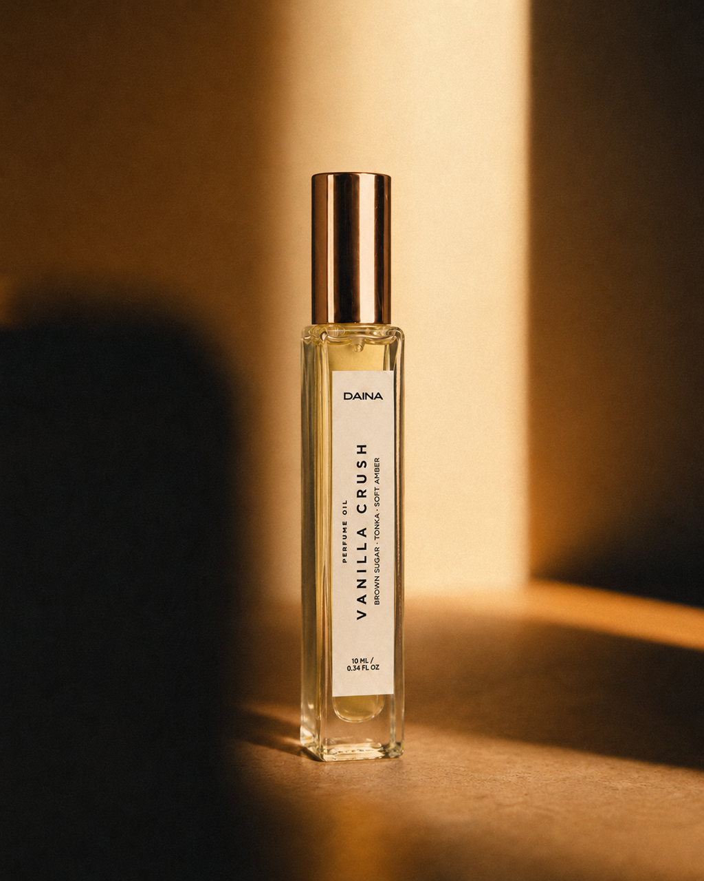 DAINA Vanilla Crush perfume bottle with gold cap in warm directional sunlight against a dark brown background