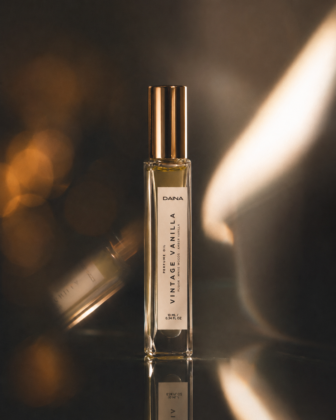 DAINA Vintage Vanilla perfume bottle with gold cap on a dark reflective surface with warm golden bokeh