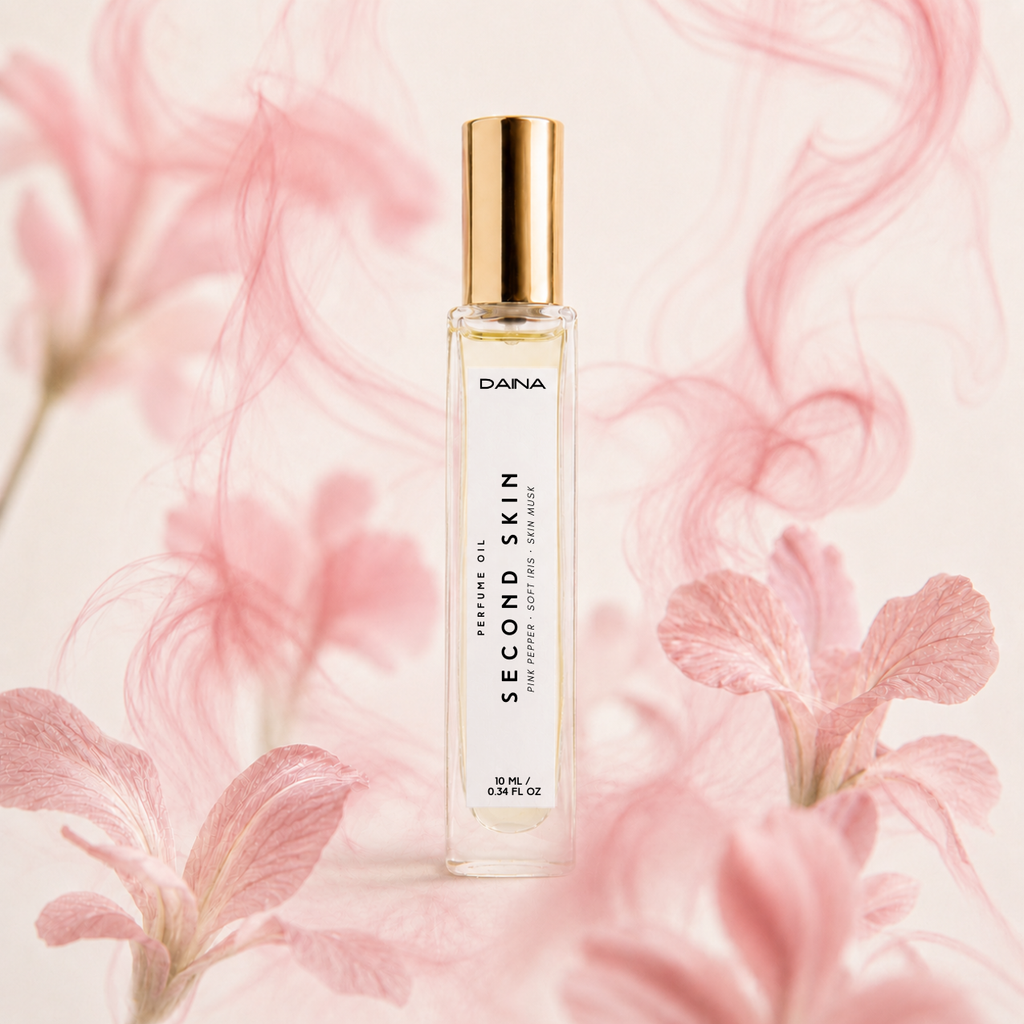 Clear rectangular bottle of DANA Second Skin perfume oil with a gold cap, set against a soft pink floral background, 10 mL